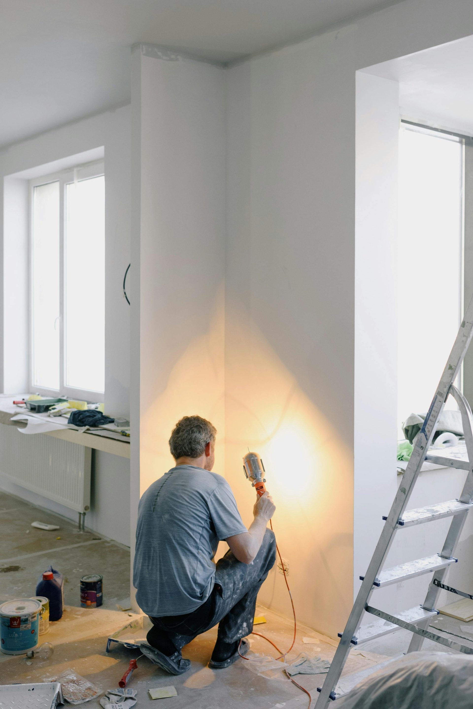 Back view of anonymous male in dirty clothes renovating walls in home while holding lamp